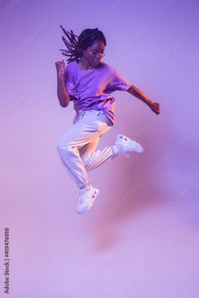 Full body of dynamic African American teen dancer leaping up while performing dance movement in bright studio Full body of dynamic African American teen dancer leaping up while performing dance movement in bright studio
