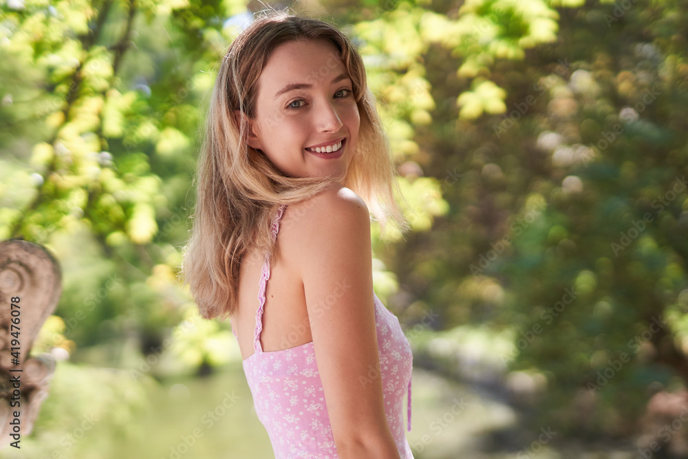 Smiling teenage female looking at camera wearing summer dress in park with green trees in Madrid Smiling teenage female looking at camera wearing summer dress in park with green trees in Madrid