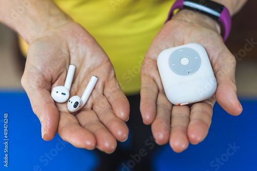 From above crop unrecognizable person wearing fitness bracelet showing wireless earbuds and modern mp3 player on hands photo