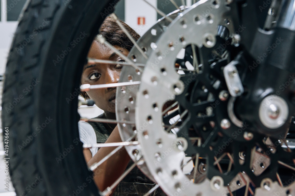 Skilled African American female mechanic fixing wheel of custom motorcycle while working in professional workshop Skilled African American female mechanic fixing wheel of custom motorcycle while working in professional workshop