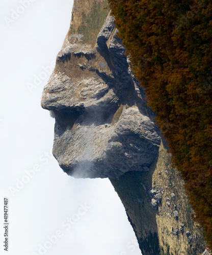 Scenic view of unusual rough mountain slope in shape of human face near lush forested terrain under clear blue sky photo