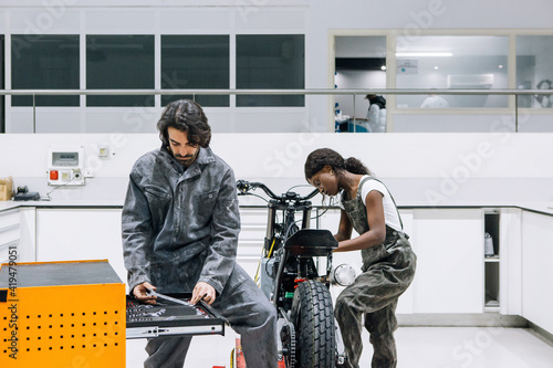 Busy multiethnic male and female technicians in dirty workwear fixing motorcycle while using instruments from tool cabinet photo