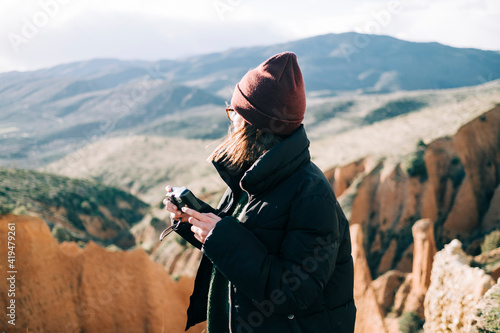 Side view of unrecognizable female tourist holding old camera while looking away standing on gorge against mount in sunlight photo