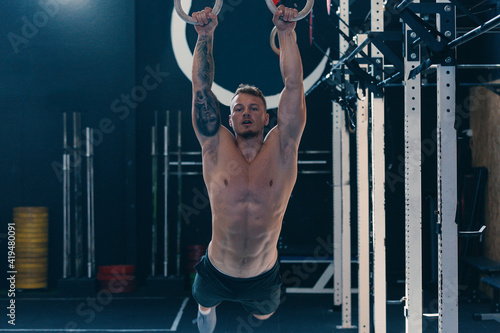 Low angle of concentrated athletic male with naked torso doing abs exercises on gymnastic rings during functional training in gym photo