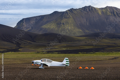 White monoplane parked on spacious grassy valley surrounded by rough picturesque mountain range in Nordic nature