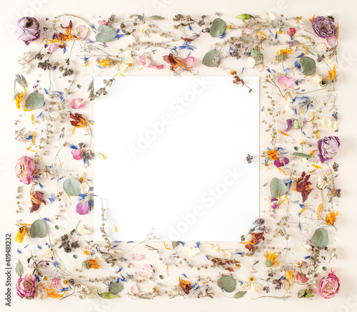Creative layout made of dried wild natural flowers and leaves and card note over pastel beige background.