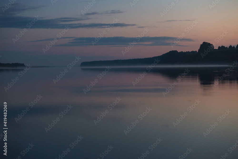 A large wild river in the summer twilight reflected the pastel tones of sunset on the water.