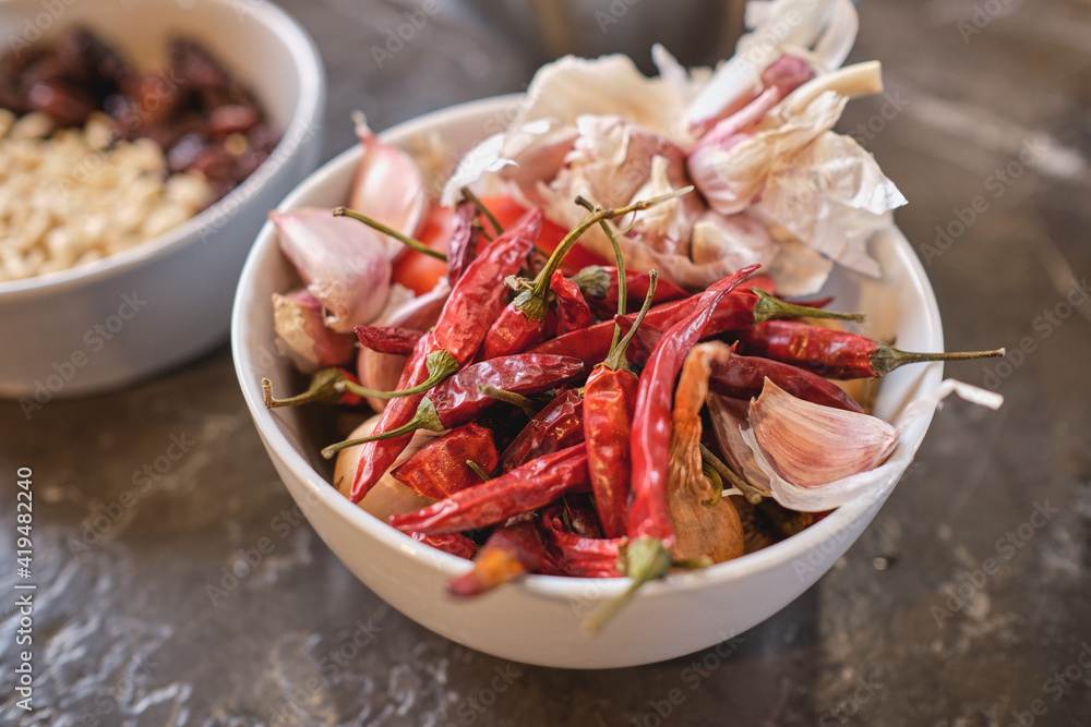 From above bowl with dried chili peppers and cloves of aromatic garlic placed on table in kitchen at home From above bowl with dried chili peppers and cloves of aromatic garlic placed on table in kitchen at home