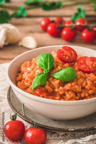 Homemade tomato risotto with fresh basil on a rustic wooden table, vertical