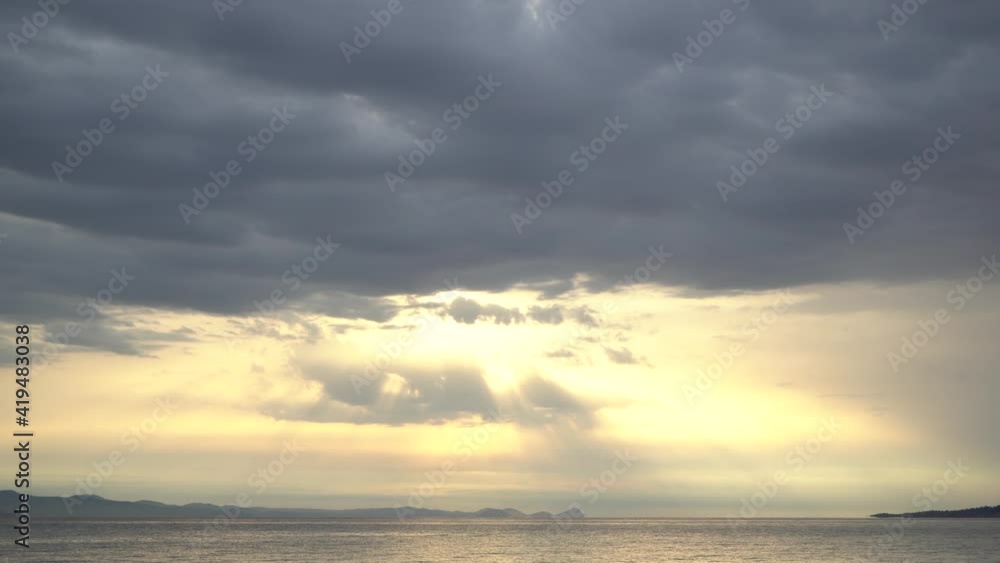 Early morning sunrise dramatic landscape. 4k stock video footage of beautiful sun shining through heavy dark grey clouds. Sea waves splash in bottom of frame Early morning sunrise dramatic landscape. 4k stock video footage of beautiful sun shining through heavy dark grey clouds. Sea waves splash in bottom of frame