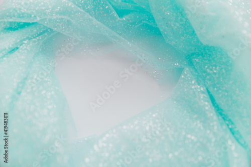 Close up picture of blue mint tulle fabric with glitter on the white background. Abstract wallpaper for the fashion industry with copy space for text. Round shape for text, flat lay.