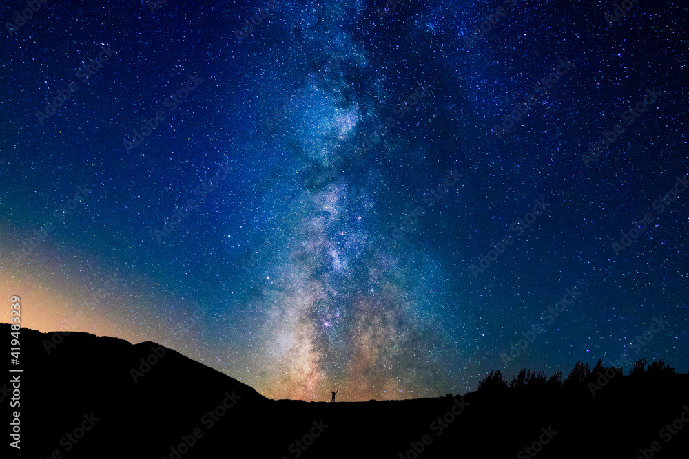 Picturesque view of starry blue sky with clouds over mount with unrecognizable person silhouettes at sunset Picturesque view of starry blue sky with clouds over mount with unrecognizable person silhouettes at sunset