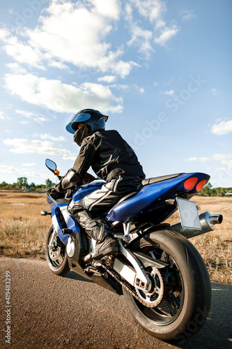 Biker or motorcyclist in a black leather suit and helmet sits on a sports motorcycle and looks into the distance. Vertical photo orientation