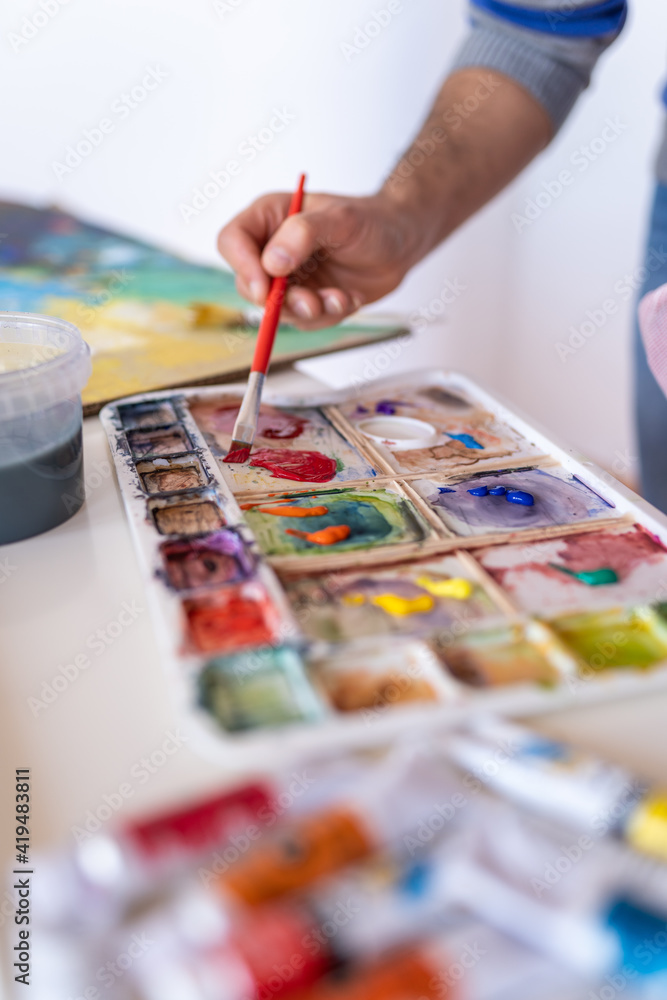 Crop anonymous male painter mixing paints with brush using watercolor palette while working in art studio Crop anonymous male painter mixing paints with brush using watercolor palette while working in art studio