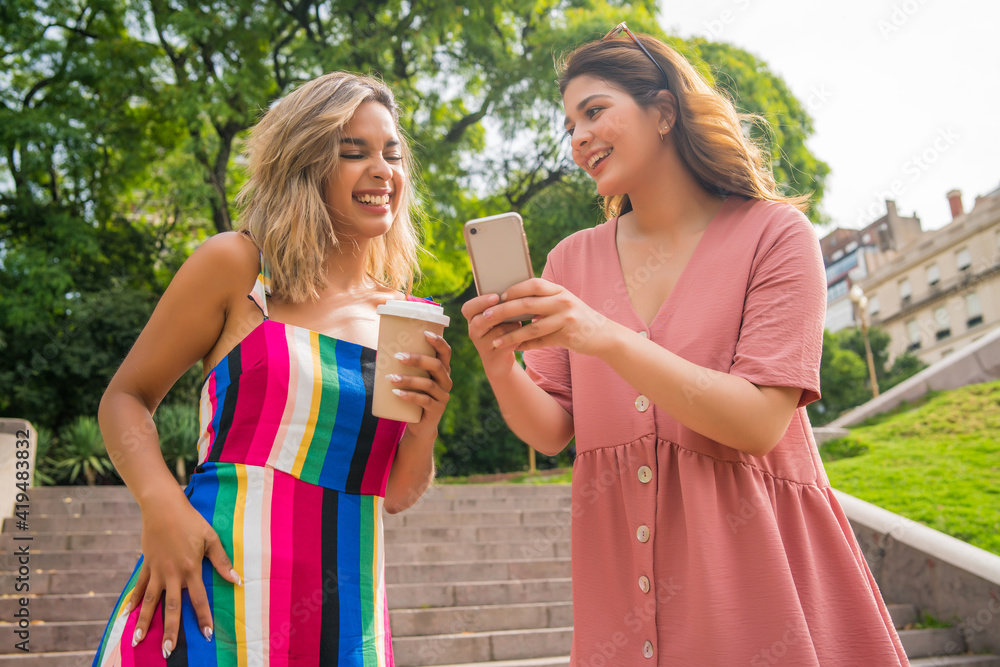 Fototapeta premium Two friends using mobile phone outdoors.