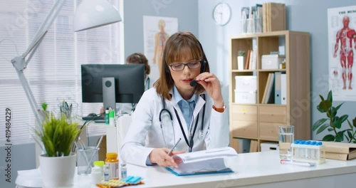 Wallpaper Mural Portrait of beautiful young Caucasian female physician sitting in hospital at desk speaking and consulting on treatment in headset with microphone on online consultation. Medical webinar medic concept Torontodigital.ca