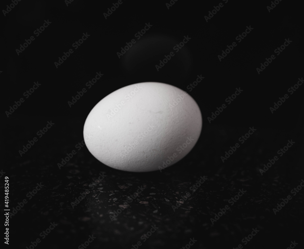 The egg is white, against a black background. Selective focus. The egg is white, against a black background. Selective focus.