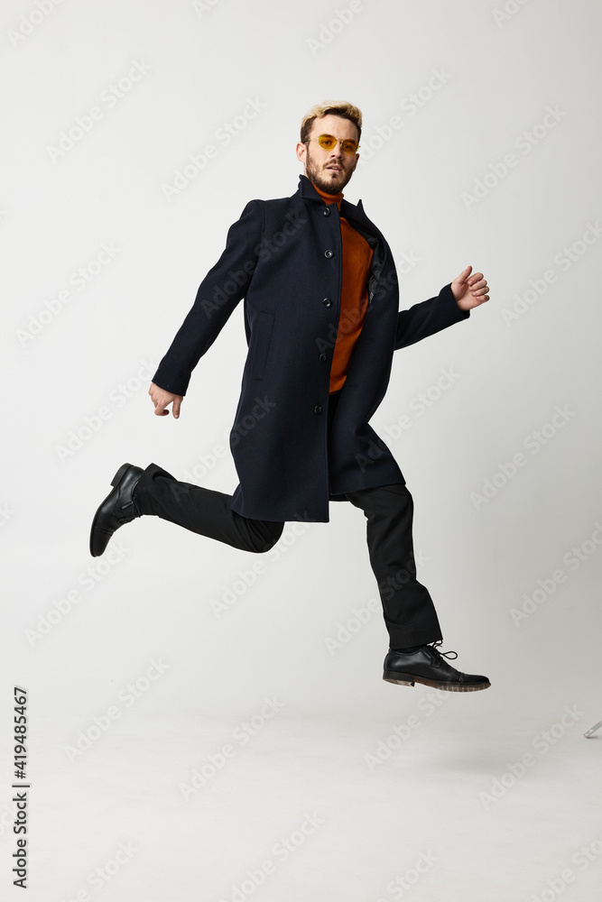 a blond man in a coat jumped up and runs to the side on a light background
