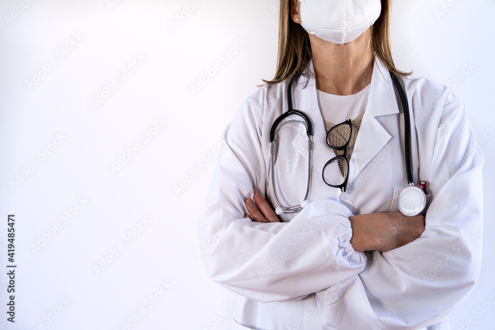 Cropped unrecognizable female doctor in white uniform and stethoscope wearing protective medical mask standing with arms crossed Cropped unrecognizable female doctor in white uniform and stethoscope wearing protective medical mask standing with arms crossed