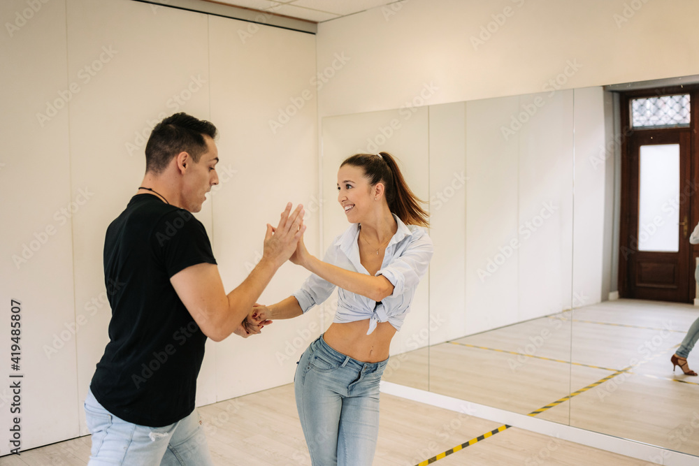 Talented couple performing ballroom dance while rehearsing in bright spacious studio with mirror during class Talented couple performing ballroom dance while rehearsing in bright spacious studio with mirror during class