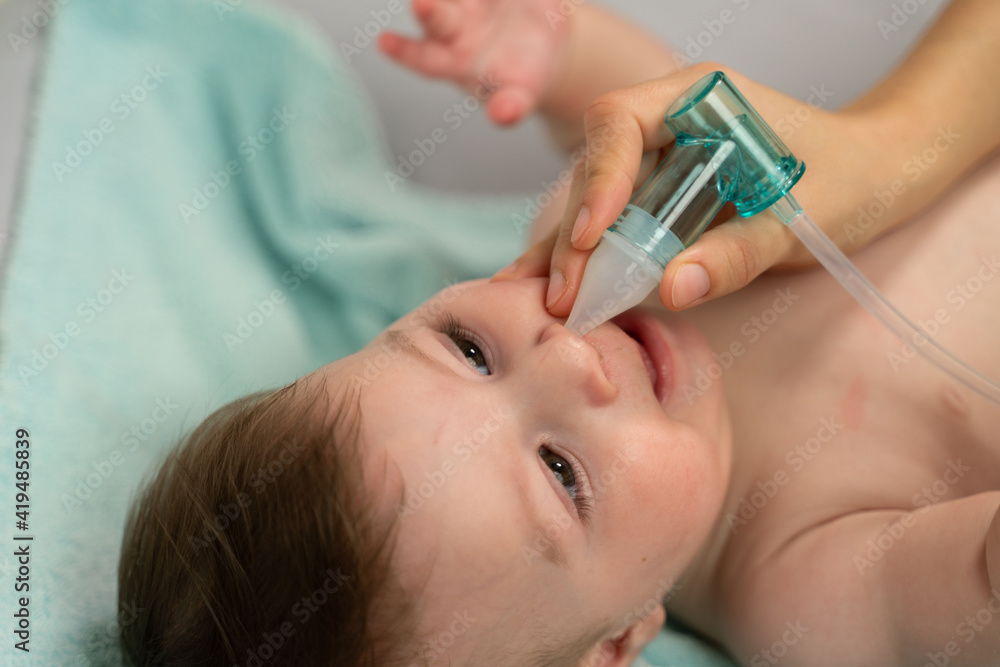 Crop caring mother placing suction machine into adorable baby nostril to remove mucus Crop caring mother placing suction machine into adorable baby nostril to remove mucus