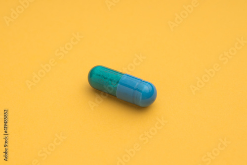 High angle of blue capsule of pharmaceutical medicinal product placed on bright yellow background photo