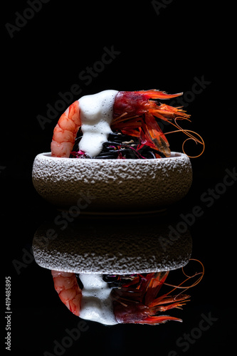 Delicious dish with prawn and sea urchin served in bowl with white sauce and placed on mirrored table in molecular gastronomy restaurant