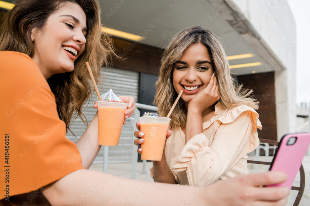 Two friends using phone at coffee shop outdoors. Two friends using phone at coffee shop outdoors.