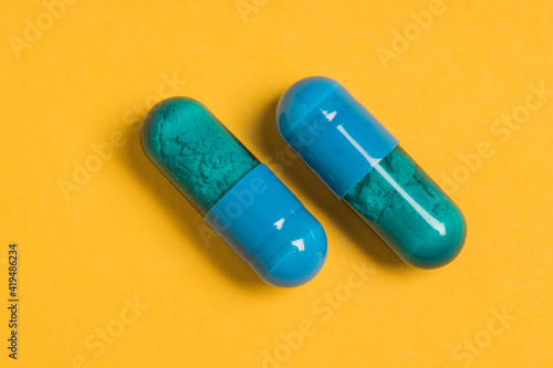 High angle of blue capsules of pharmaceutical medicinal product placed on bright yellow background