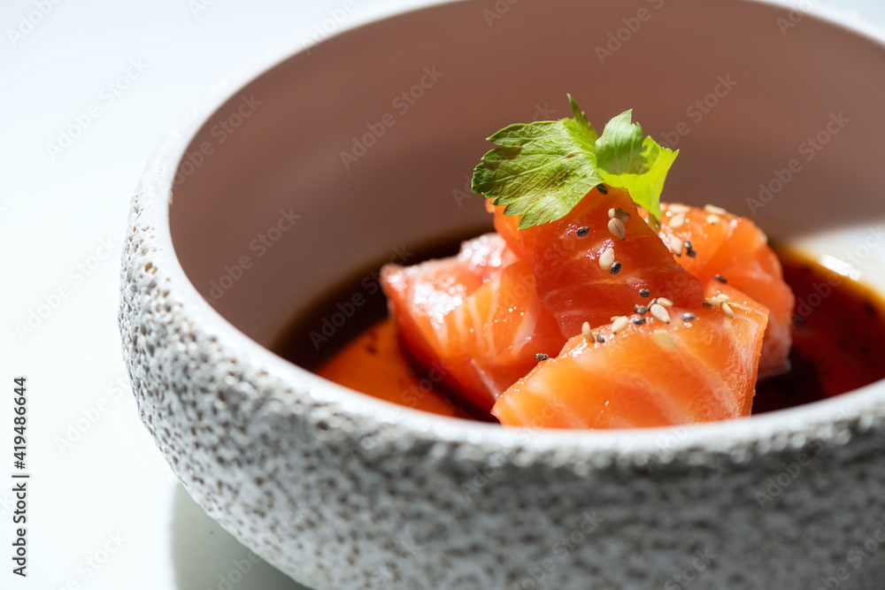 From above of delicious raw salmon sashimi with soy sauce served in stylish bowl and placed on white table From above of delicious raw salmon sashimi with soy sauce served in stylish bowl and placed on white table