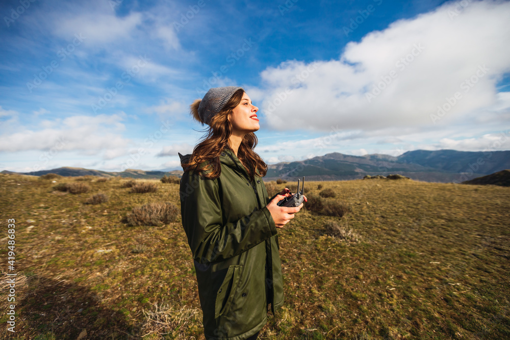 Young female tourist with pouting lips controlling UAV with remote controller while looking away on lawn in Europe Young female tourist with pouting lips controlling UAV with remote controller while looking away on lawn in Europe