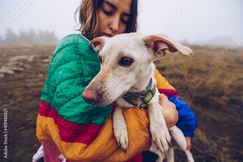 Side view of loving female owner kissing adorable white dog during stroll in nature on foggy day photo