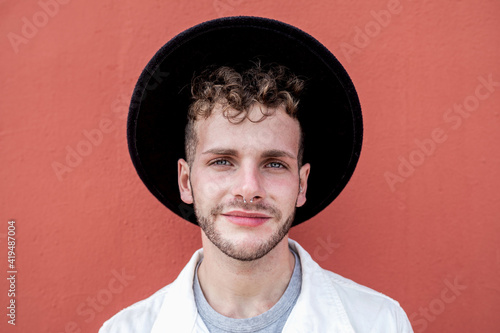 Cheerful young male millennial in stylish clothes smiling while resting on street against red wall photo