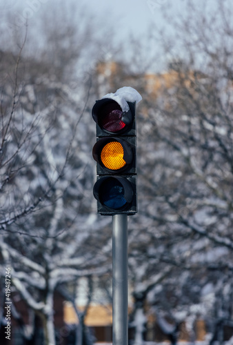 Amber traffic light on metal post against leafless trees in town in cold weather