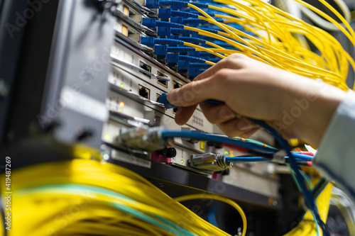 From below of crop anonymous man putting electronic cable in data system in communications room