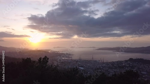 Aerial view of the coast city of Vigo in the atlantic ocean at sunset with the natural park of the Cies island in the background. Drone stablishing shot forward travelling photo