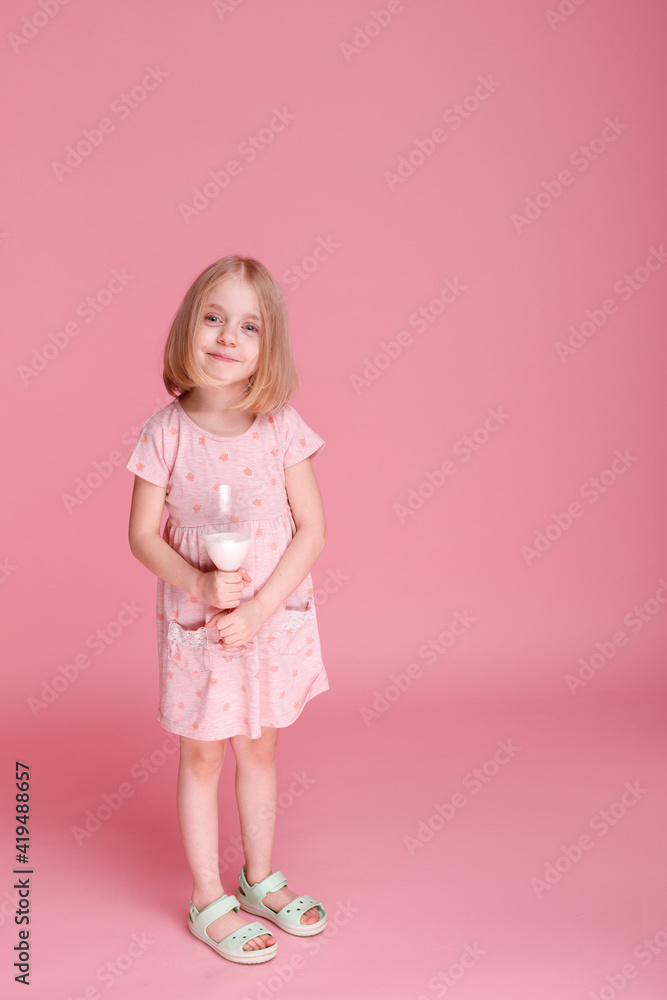 Little girl in dress and glass of milk on pink background