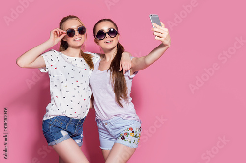 Young happy smiling friends women posing isolated over pink wall background take selfie.