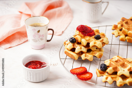 Delicious breakfast table, waffles with berries, jam and cup of coffee. Front view. Marble background. High quality photo. Selective focus. 
