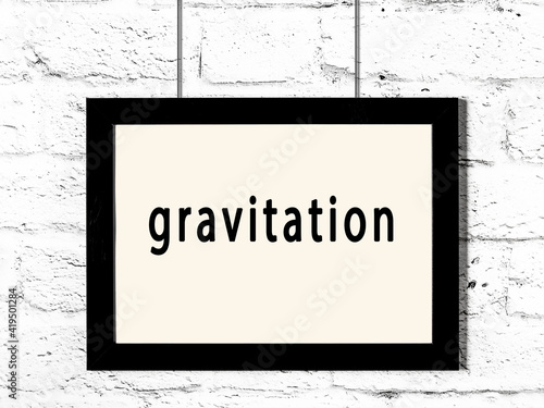 Fototapeta Black frame hanging on white brick wall with inscription gravitation