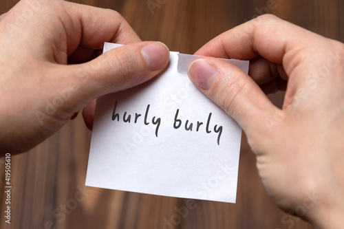 Hands of a man tearing a piece of paper with inscription hurly burly photo