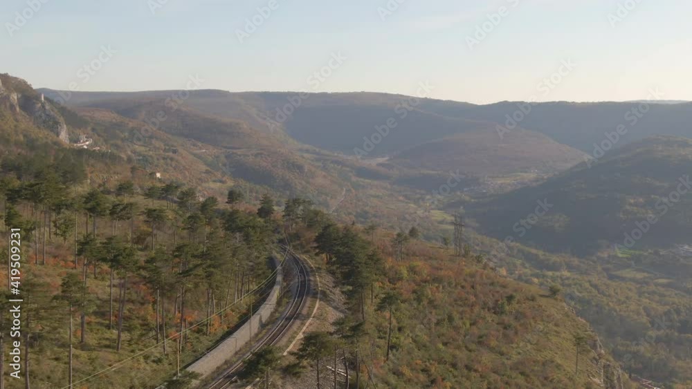 DRONE: Flying above an empty steel railway running across the picturesque autumn colored countryside in Slovenia. Train tracks run along a hill overlooking the forest covered valley near Crni Kal DRONE: Flying above an empty steel railway running across the picturesque autumn colored countryside in Slovenia. Train tracks run along a hill overlooking the forest covered valley near Crni Kal