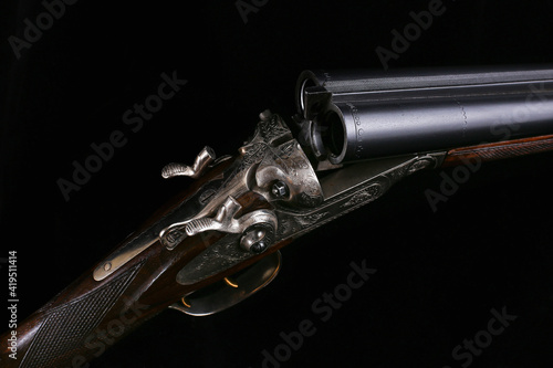 Details of an elegant double-barreled hunting classic shotgun on a black background close-up finished with a pattern for metal and carving on a wooden butt. Macro photography