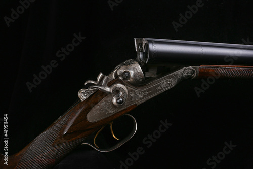 Details of an elegant double-barreled hunting classic shotgun on a black background close-up finished with a pattern for metal and carving on a wooden butt. Macro photography