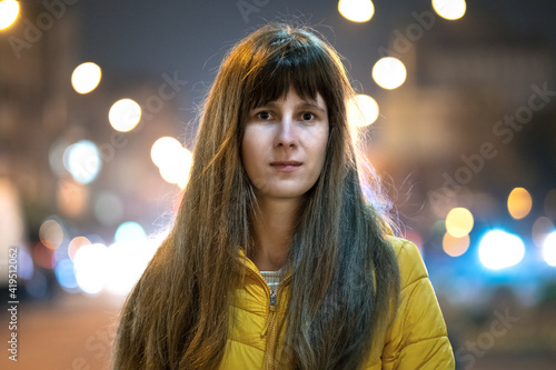 Portrait of young woman standing outdoors on city street at night.