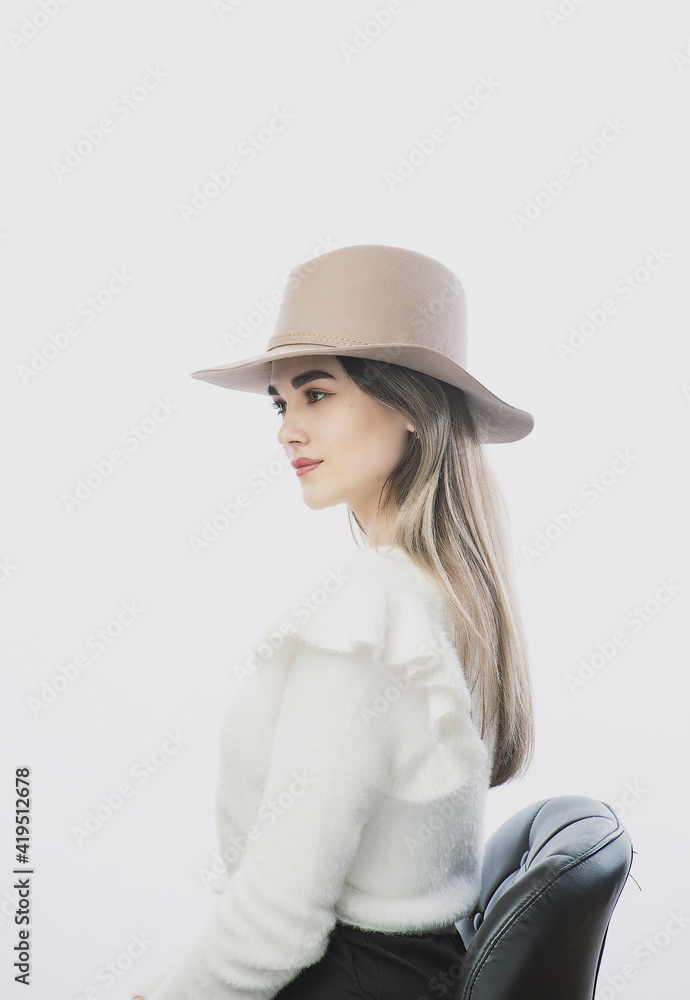 girl in a white sweater posing in a felt hat on a light background