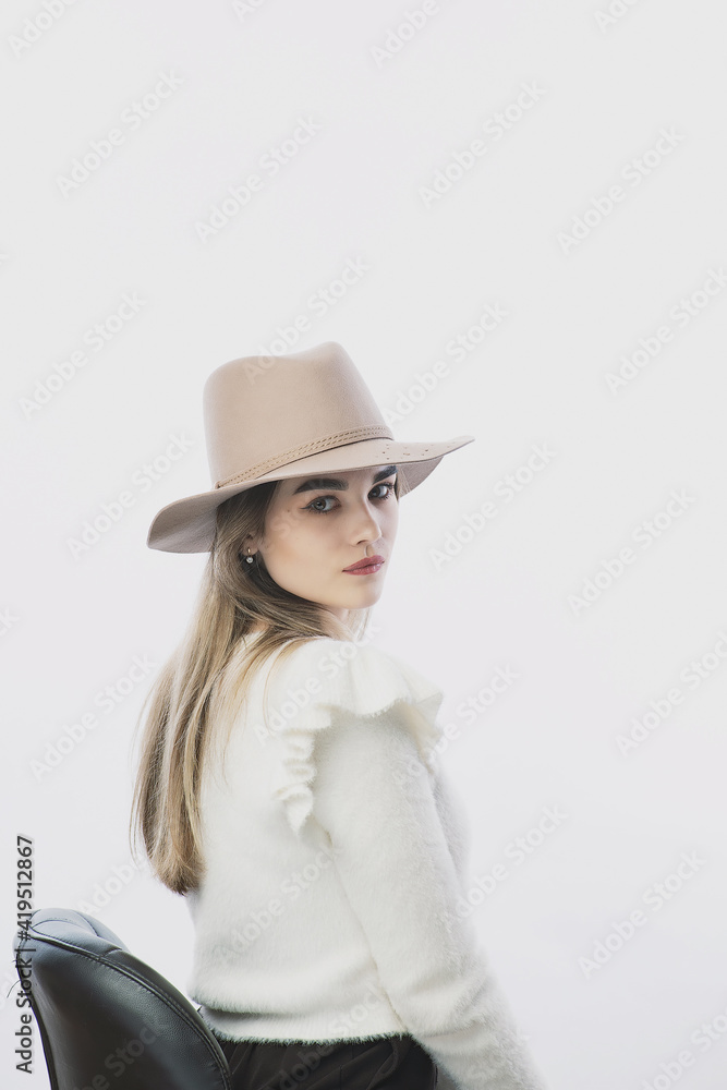 girl in a white sweater posing in a felt hat on a light background girl in a white sweater posing in a felt hat on a light background