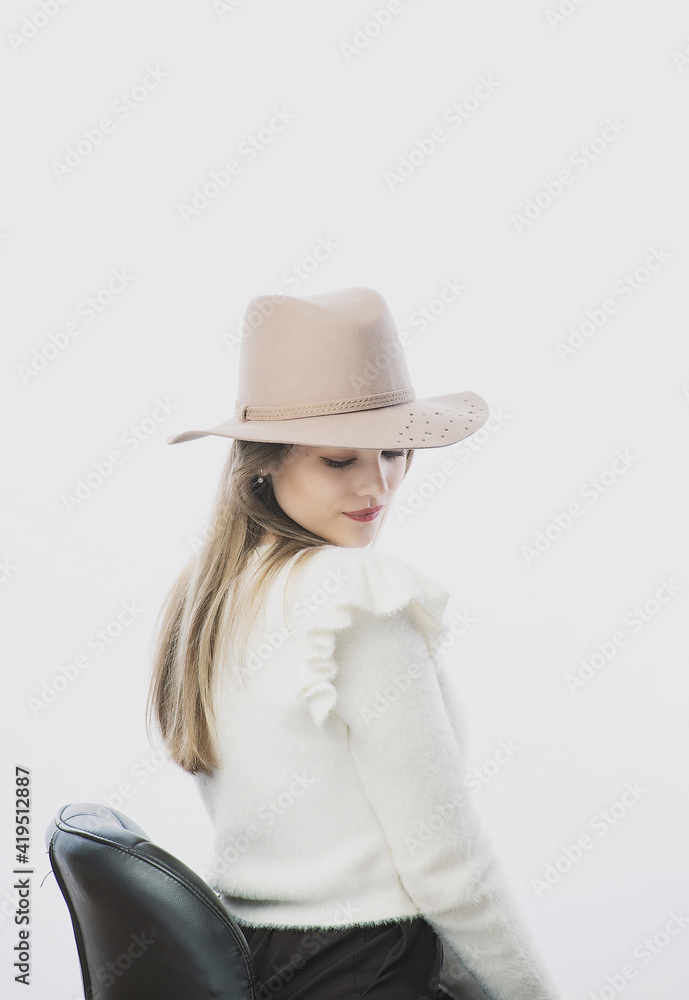 girl in a white sweater posing in a felt hat on a light background girl in a white sweater posing in a felt hat on a light background