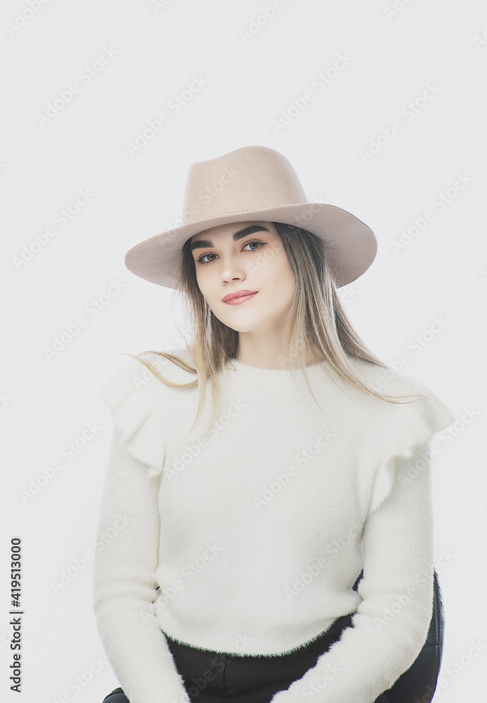 girl in a white sweater posing in a felt hat on a light background