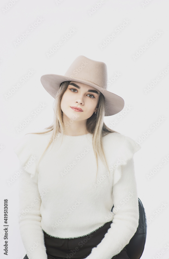 girl in a white sweater posing in a felt hat on a light background